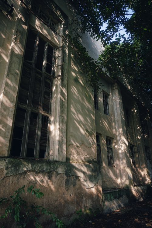 Free Rustic and eerie facade of an abandoned building surrounded by trees casting intricate shadows. Stock Photo
