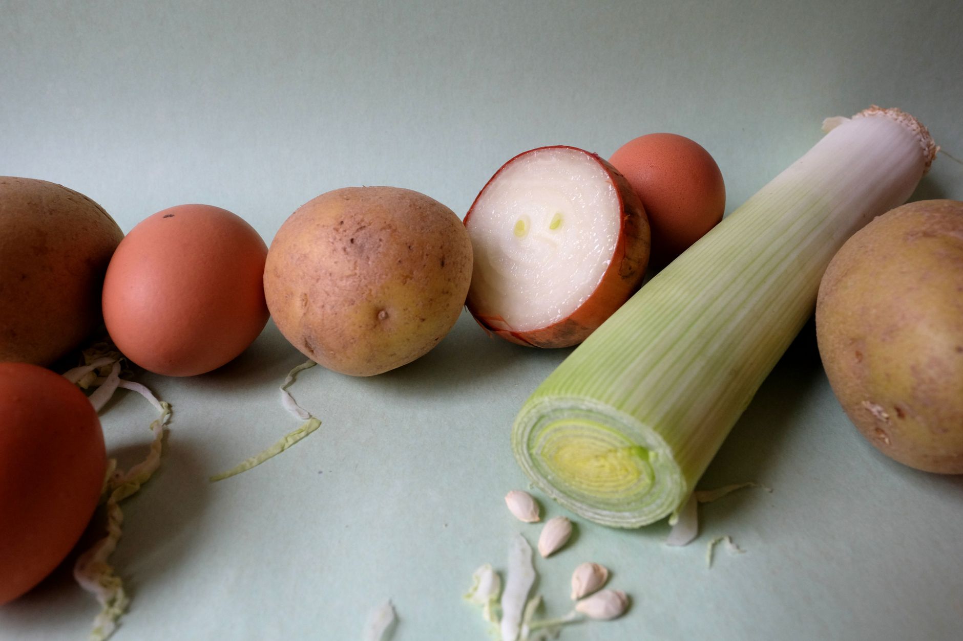Potatoes, eggs, onion, and leek arranged on a light background.