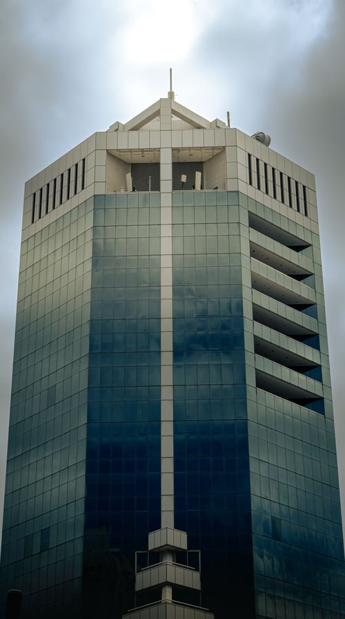Free Tall modern skyscraper with reflective glass facade under a dramatic cloudy sky. Stock Photo