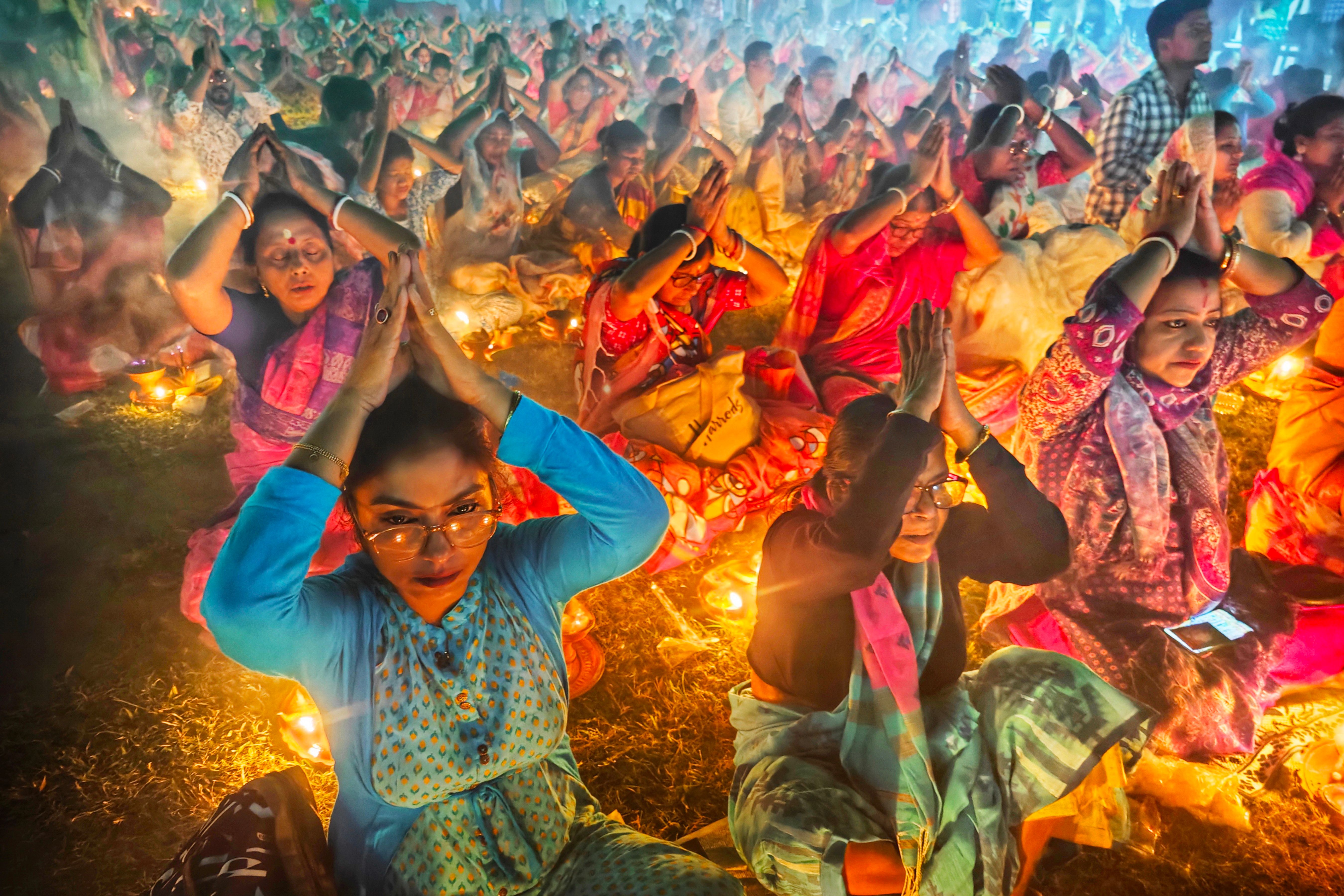 Women in traditional sarees participate in a vibrant outdoor prayer ceremony in Kolkata, India.