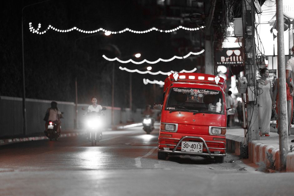 An eye-catching red vehicle stands out on a lively city street at night, surrounded by traffic and lights.
