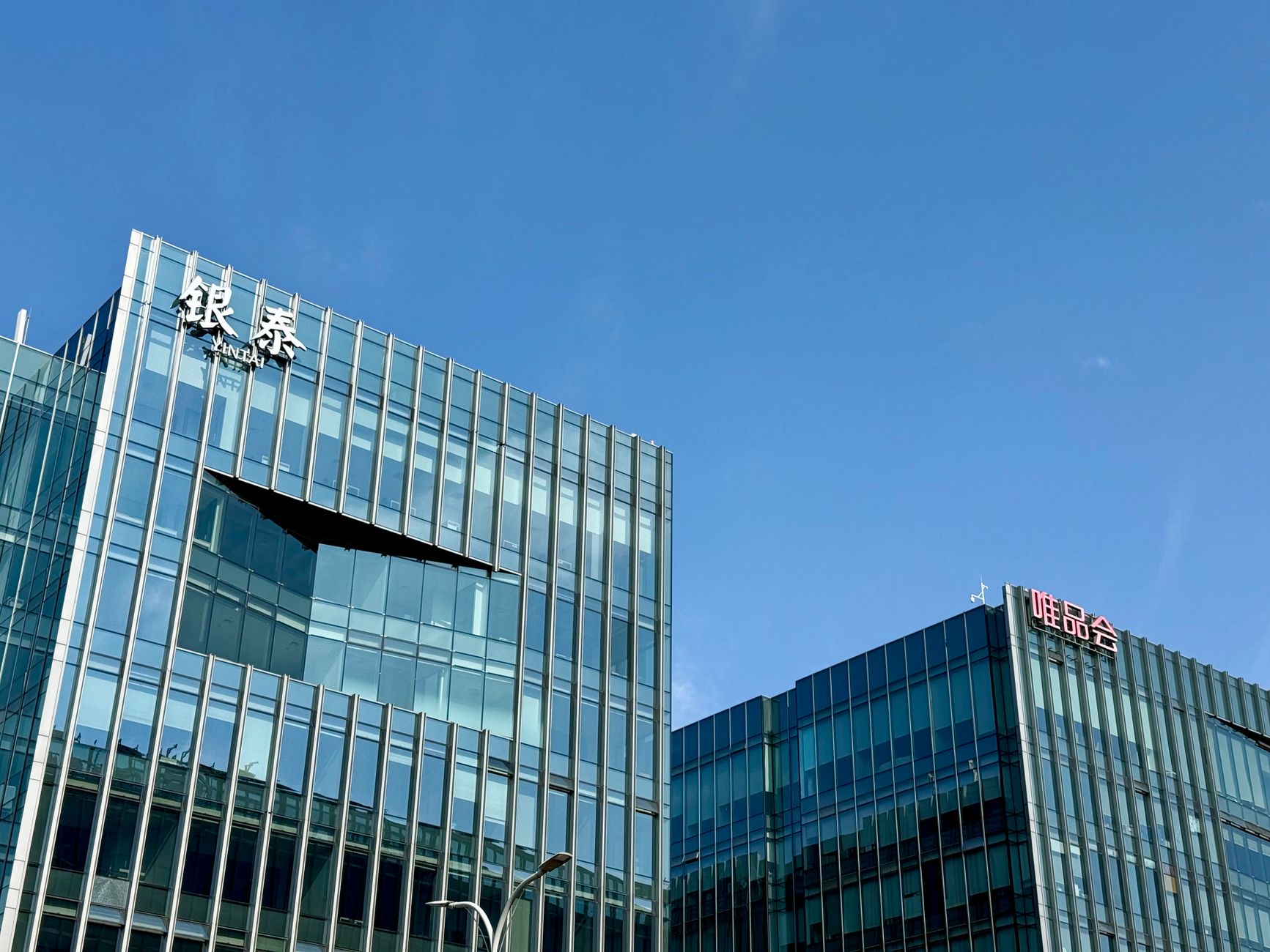 Close-up of modern glass facade buildings under a clear blue sky in Shanghai, China.