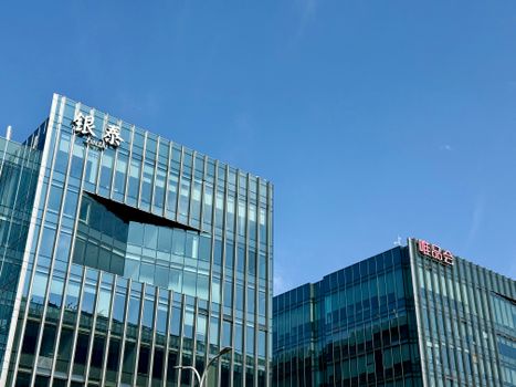 Close-up of modern glass facade buildings under a clear blue sky in Shanghai, China.