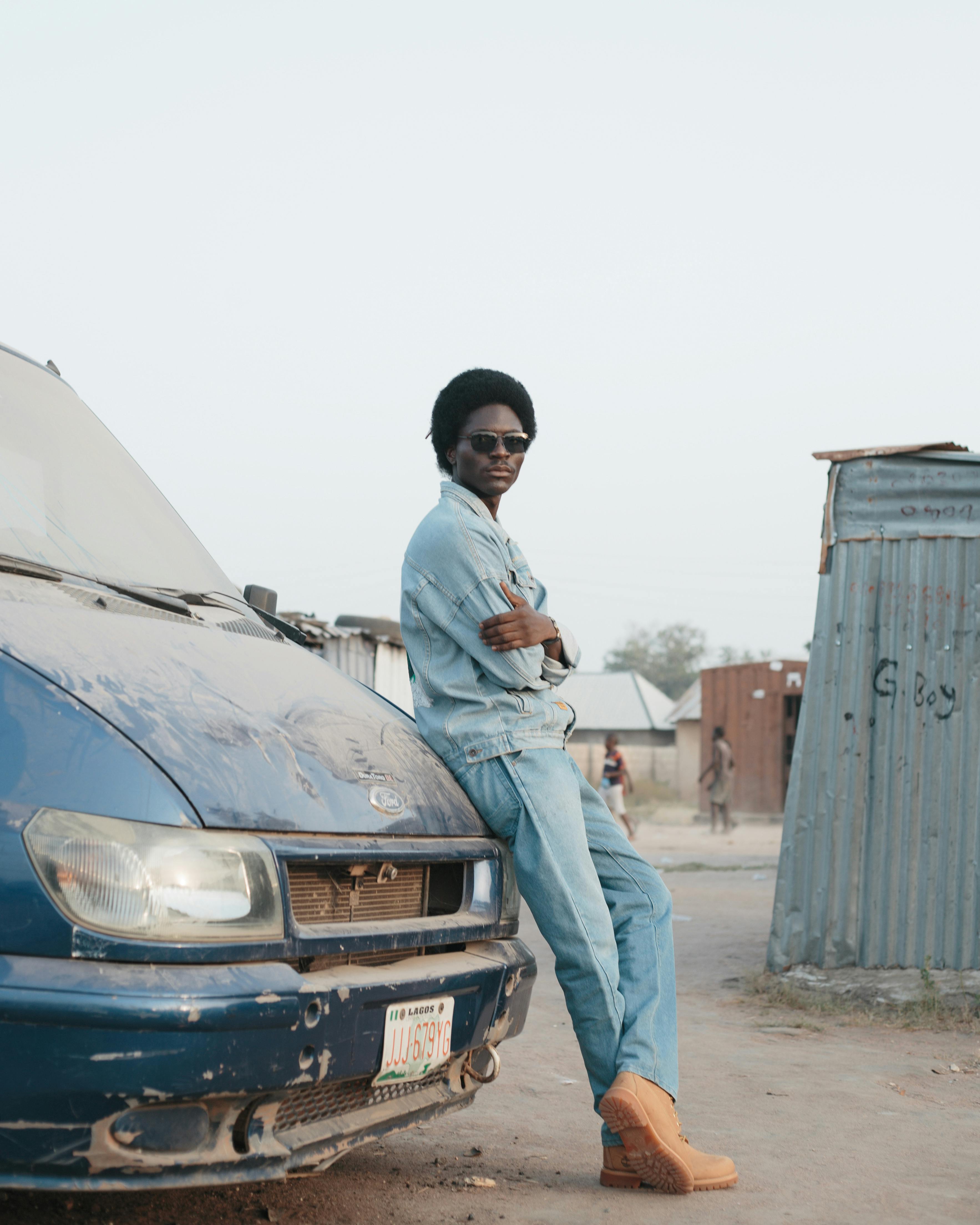 De franc Home amb vestit texà recolzat en una furgoneta blava polsegosa en un entorn urbà. Foto d'estoc