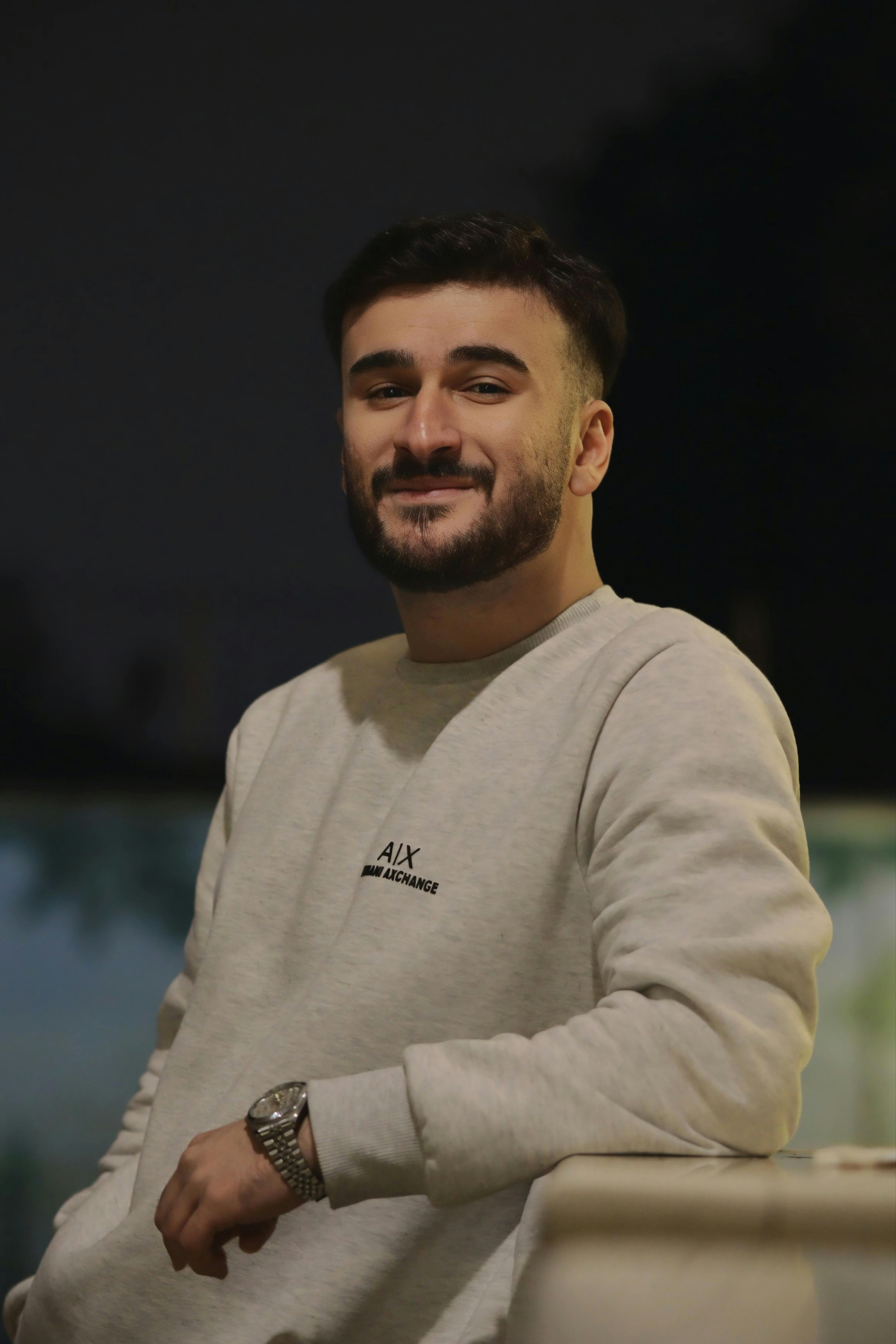 A young man in a sweatshirt smiles warmly during an outdoor evening shoot.