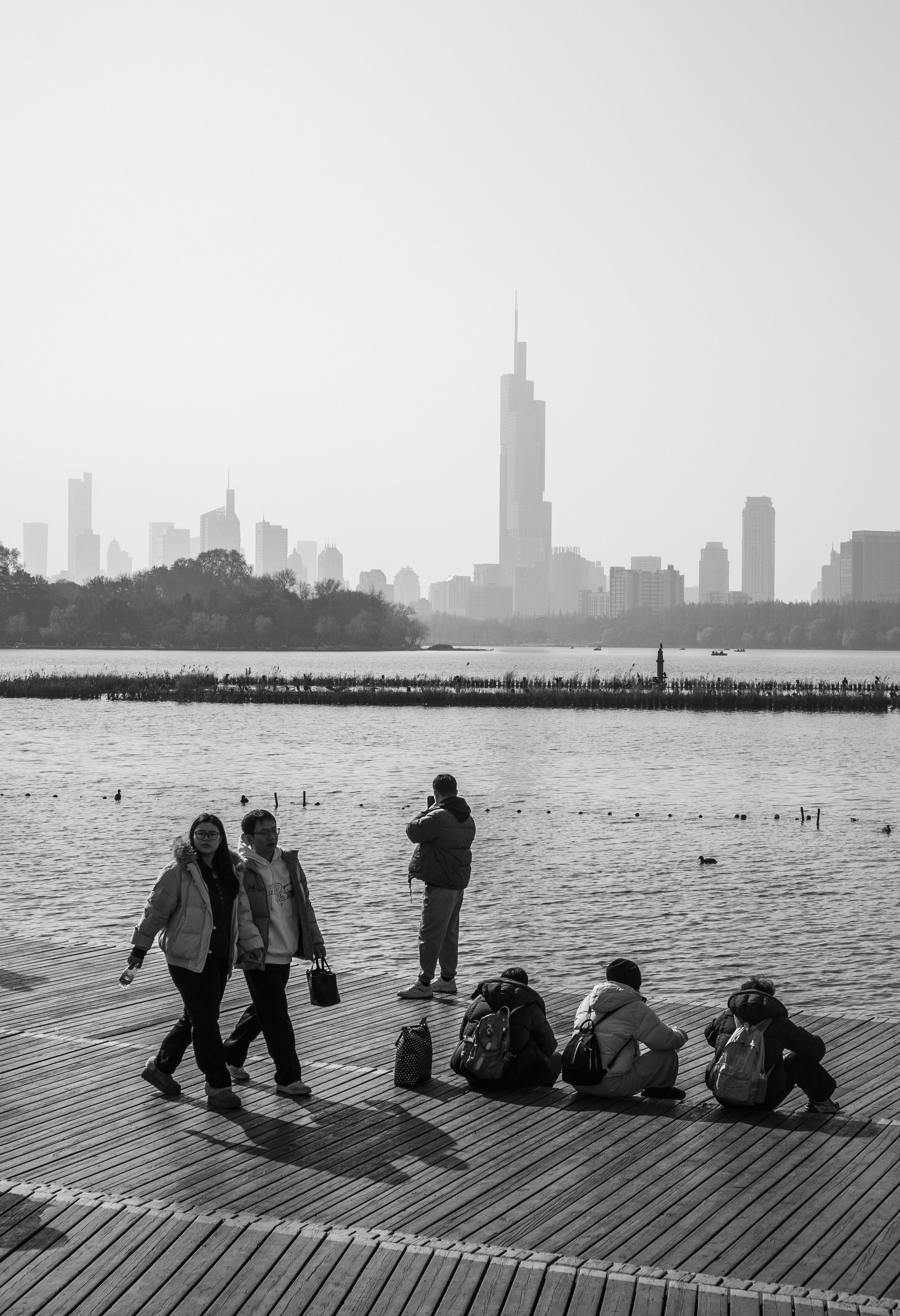 Scenic black and white view of Nanjing's skyline from a lakeside boardwalk.