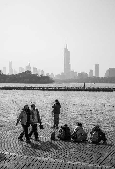 Scenic black and white view of Nanjing's skyline from a lakeside boardwalk.