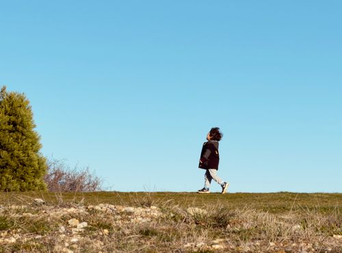Free A child walks along a grassy field under a clear blue sky in Greece. Stock Photo