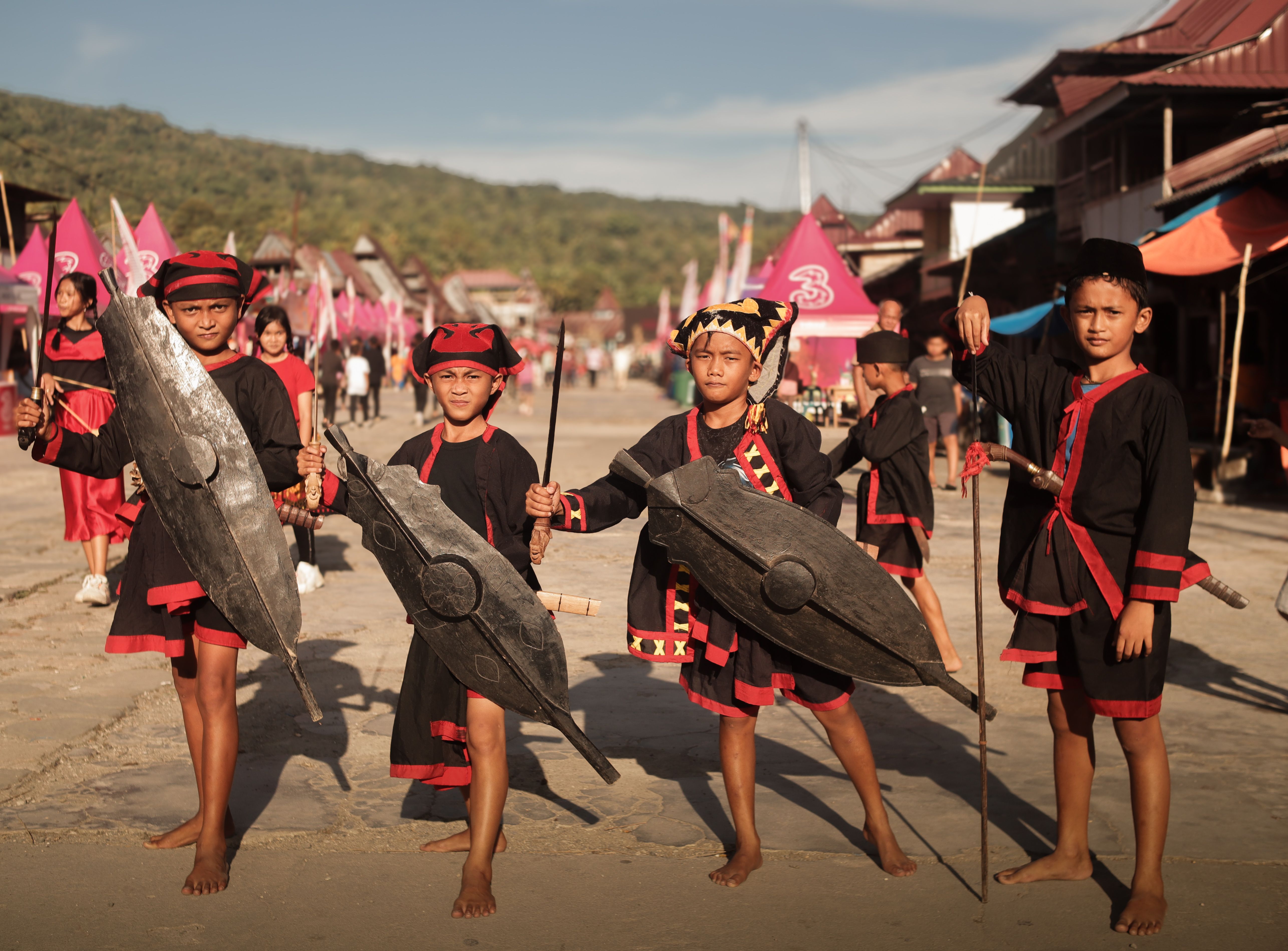 A Southeast Asian village festival displaying traditional rooster paintings beside wooden farming tools