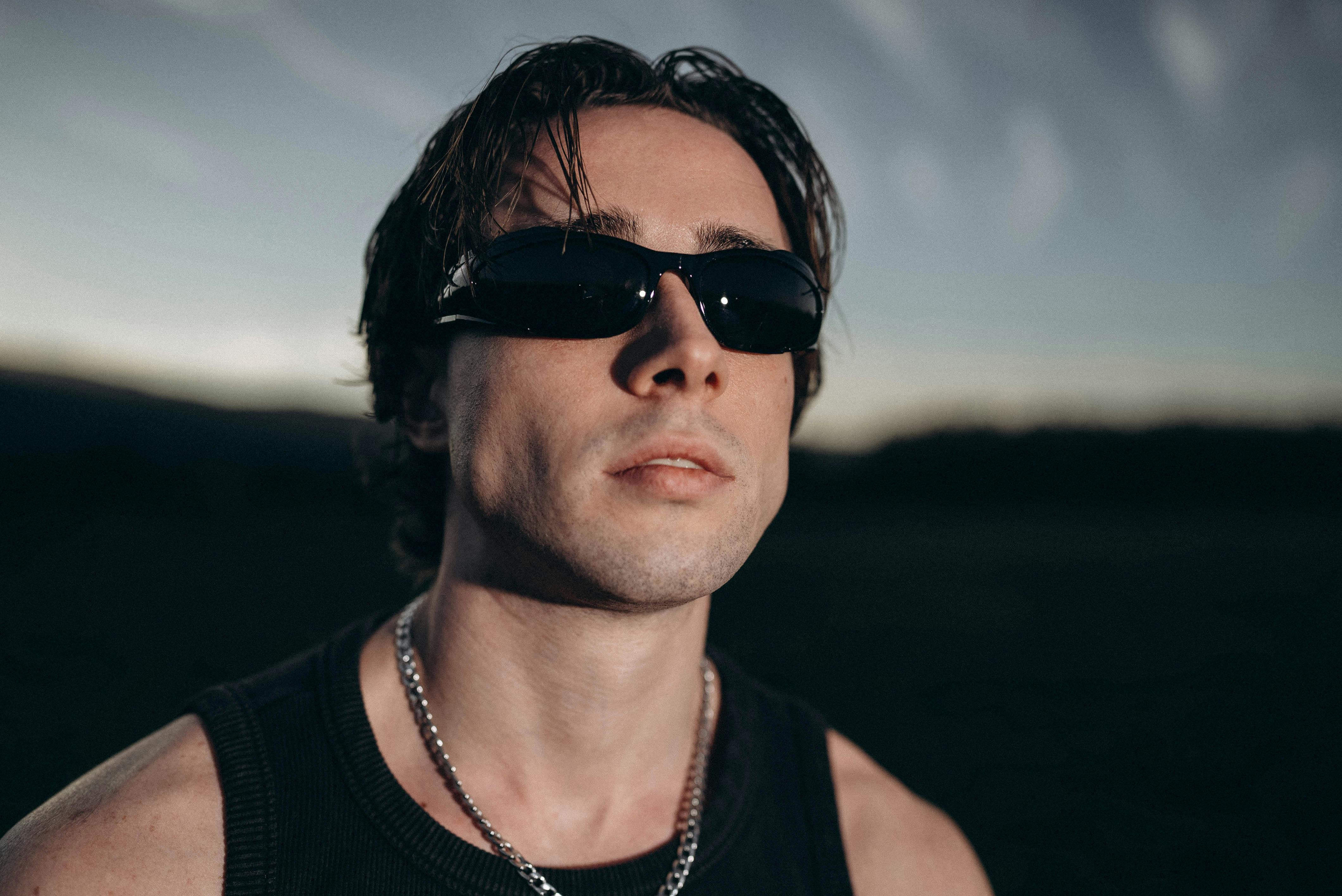 Portrait of a stylish man wearing sunglasses and a chain necklace, captured during sunset outdoors.