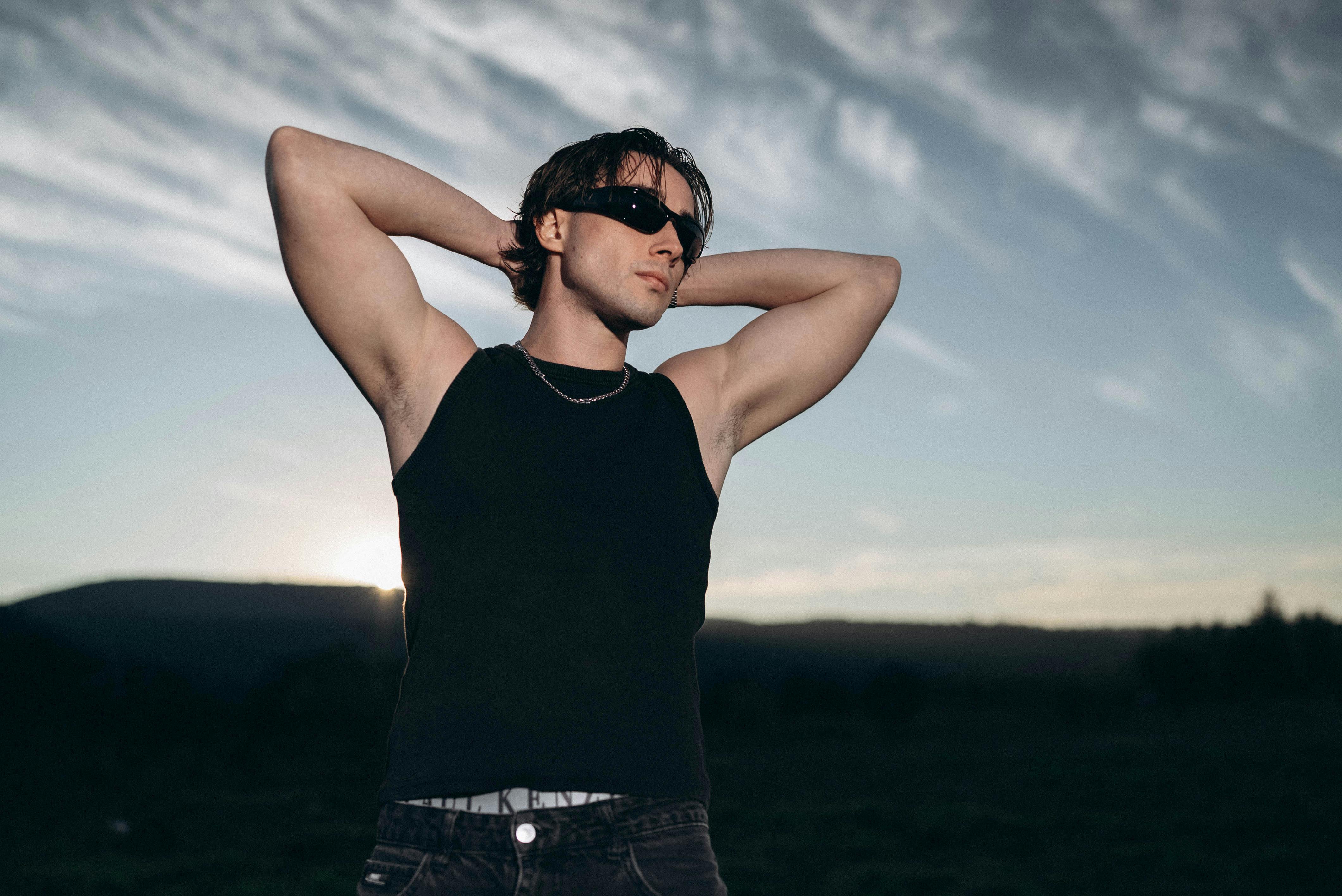 Kostenlos Junger Mann mit Sonnenbrille posiert selbstbewusst im Freien bei Sonnenuntergang und versprüht eine moderne und stilvolle Ausstrahlung. Stock-Foto