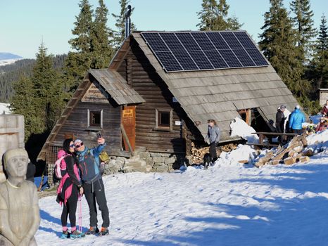 Hikers taking a selfie near a snow-covered cabin with solar panels.