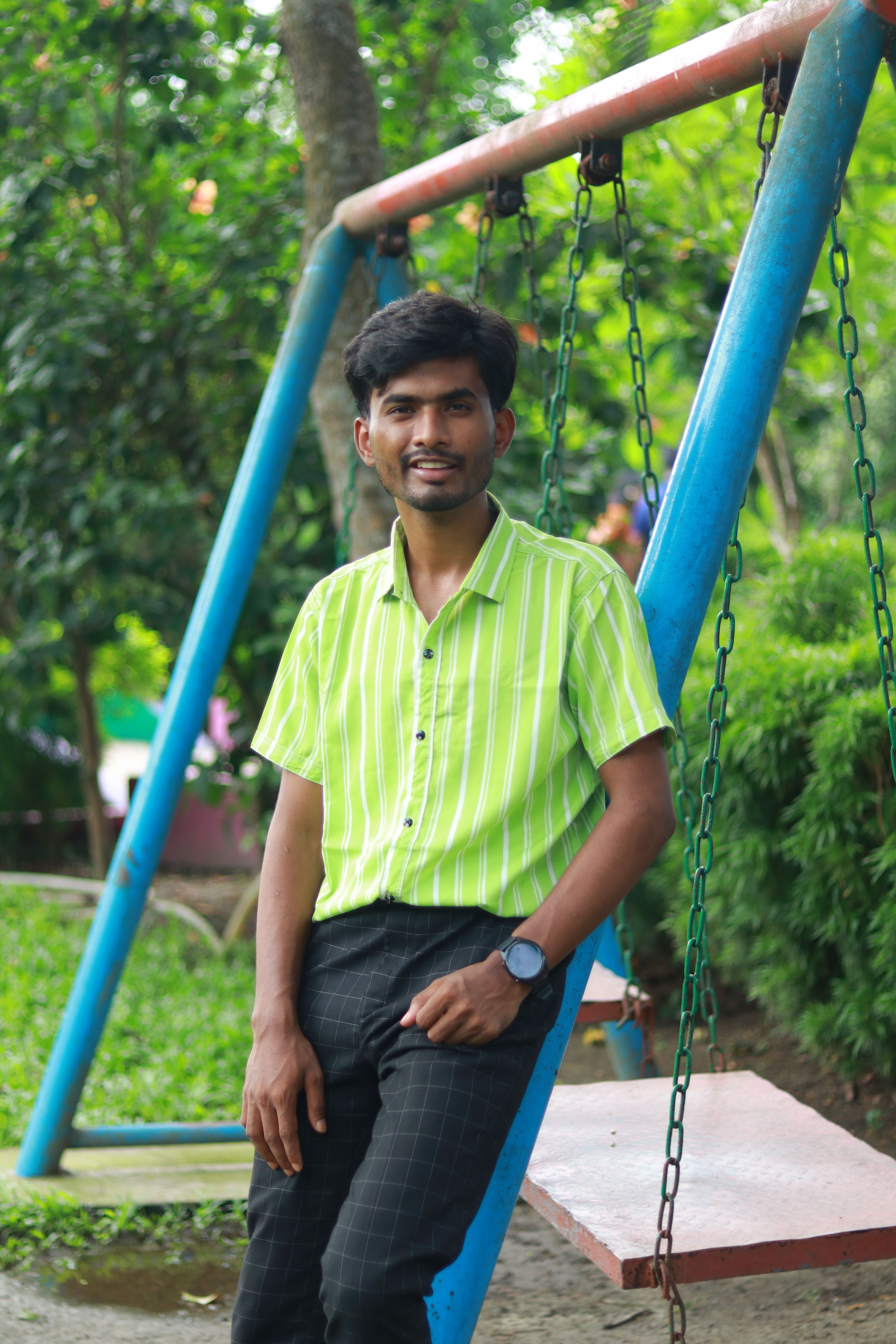 Casual young man relaxing on a swing in a lush green park setting.