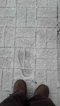Footsteps in fresh snow with brown boots on a paved path capturing a winter day.