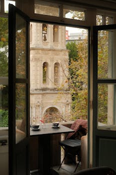 A cozy view of an Istanbul tower framed by an open window with autumn foliage.