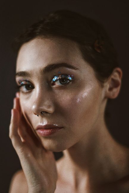 Beautiful portrait of a woman with glitter makeup accentuating her expressive eyes, set in a moody atmosphere.