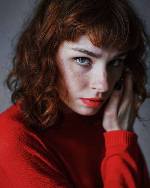 Close-up portrait of a freckled woman with curly hair in a red sweater in Kyiv.