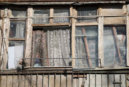 Aged wooden windows with lace curtains and peeling paint in Nikopol, Ukraine.