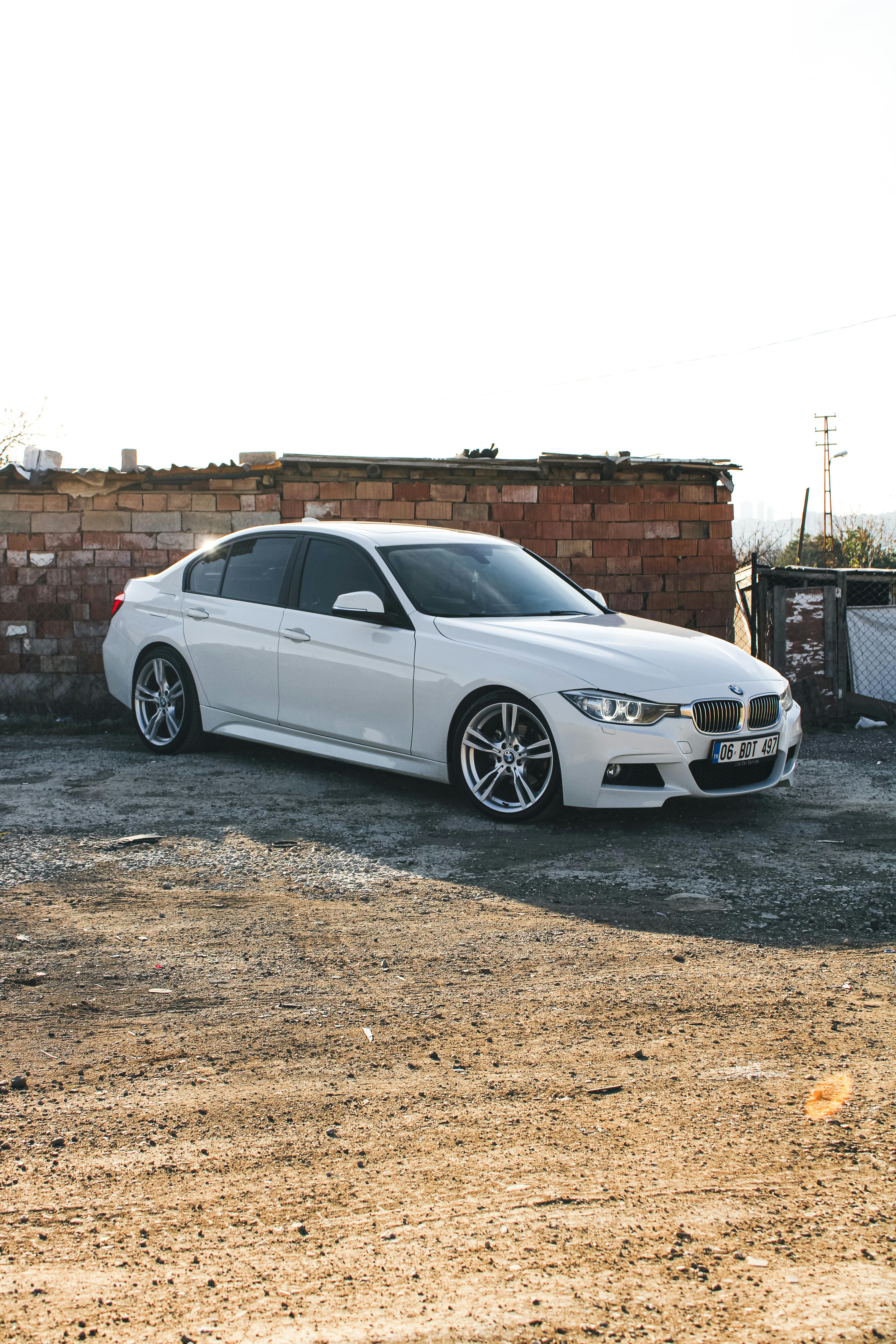 Free White sedan parked outdoors on a sunny day in an urban setting with brick wall background. Stock Photo