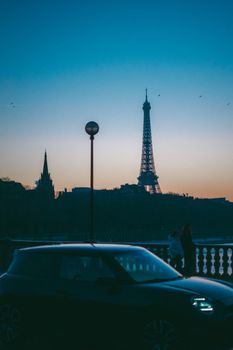 Silhouette of Eiffel Tower against twilight sky with car and streetlamp in foreground.