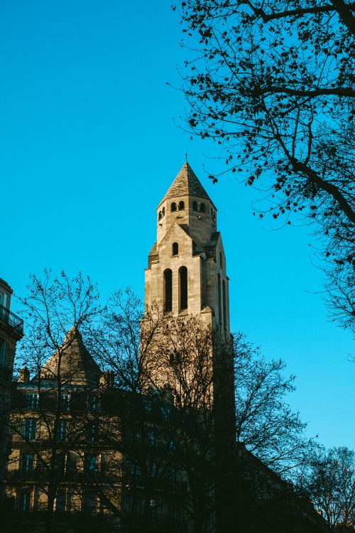 Free Beautiful Gothic architectural tower set against a vibrant blue sky with silhouetted branches. Stock Photo