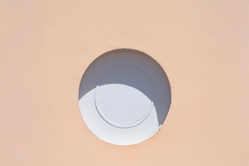 Free A minimalist photo of a circular architectural detail against a peach wall, casting a shadow. Stock Photo