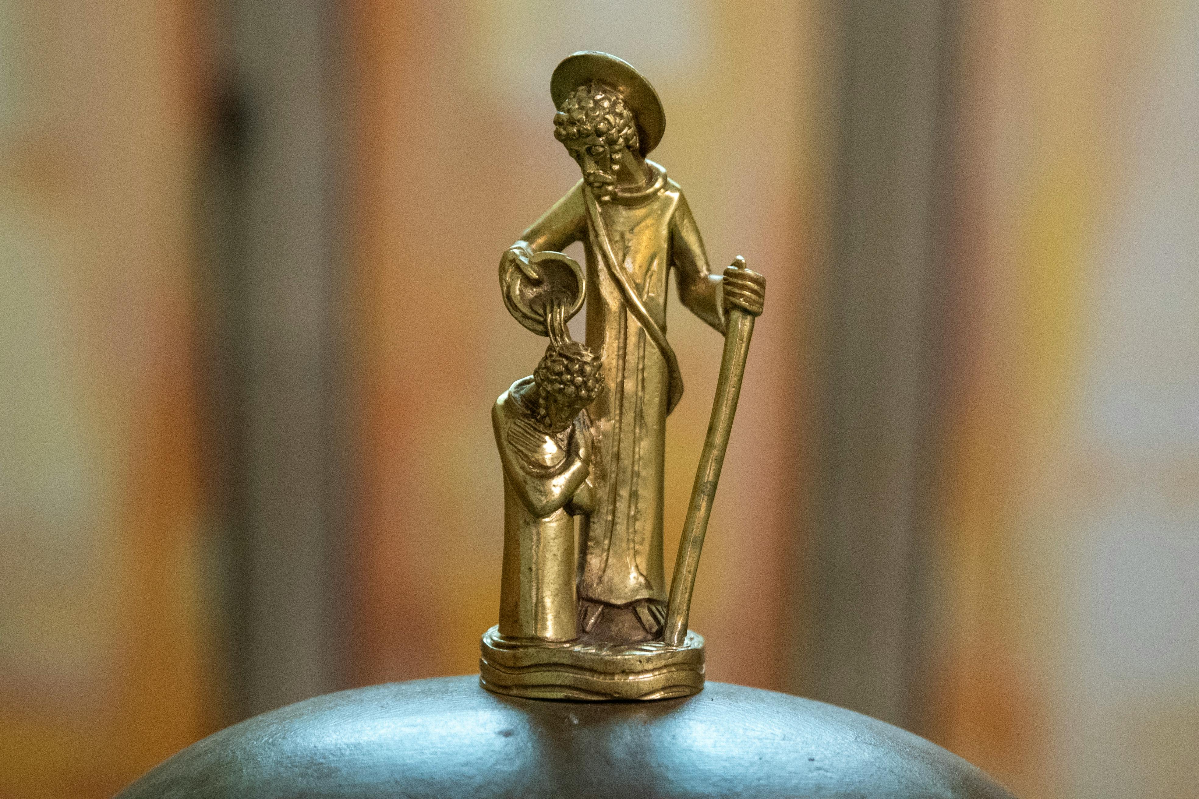 Close-up of a golden baptism sculpture depicting a religious scene indoors.