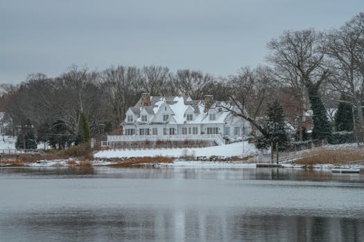 Elegant mansion by the lake surrounded by snow and winter trees.