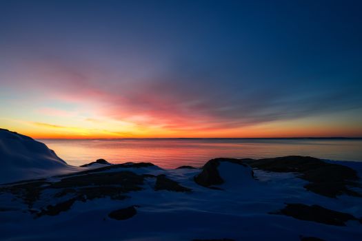 Vivid sunset over an icy shoreline, showcasing winter's tranquil beauty and colorful sky.