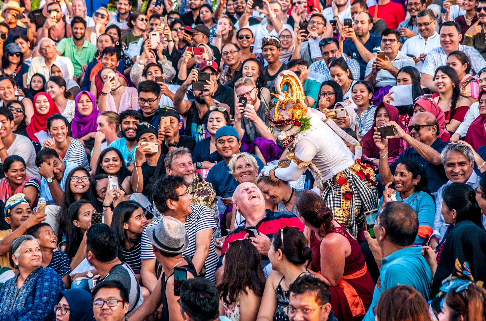 Balinese cockfight arena crowded with villagers, handlers holding roosters, tropical afternoon atmosphere