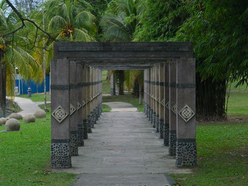 Free A serene stone pergola walkway surrounded by palm trees and greenery in a tropical park. Stock Photo