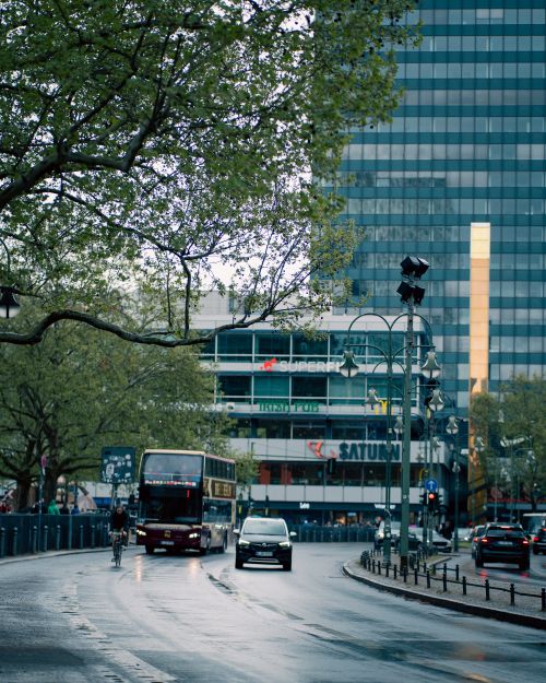 Free Rainy day in Berlin featuring a double-decker bus, cyclists, and urban architecture in a bustling city scene. Stock Photo