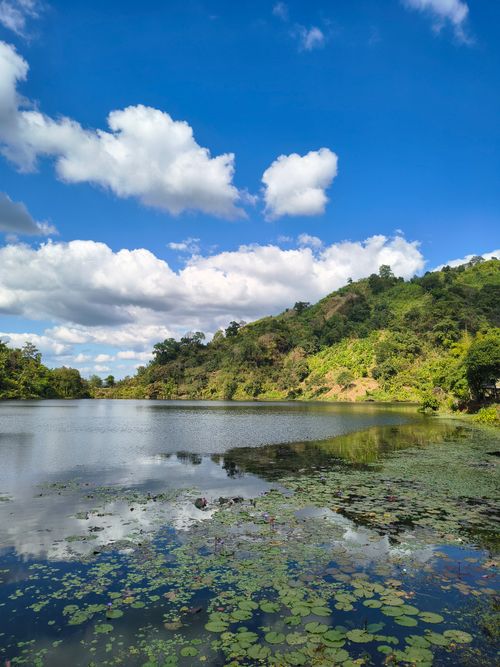 Free A tranquil mountain lake with lush greenery and cloudy blue sky reflecting on the water. Stock Photo