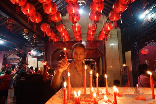 Free An elderly man lights candles underneath red lanterns in an ornate Chinese temple setting. Stock Photo