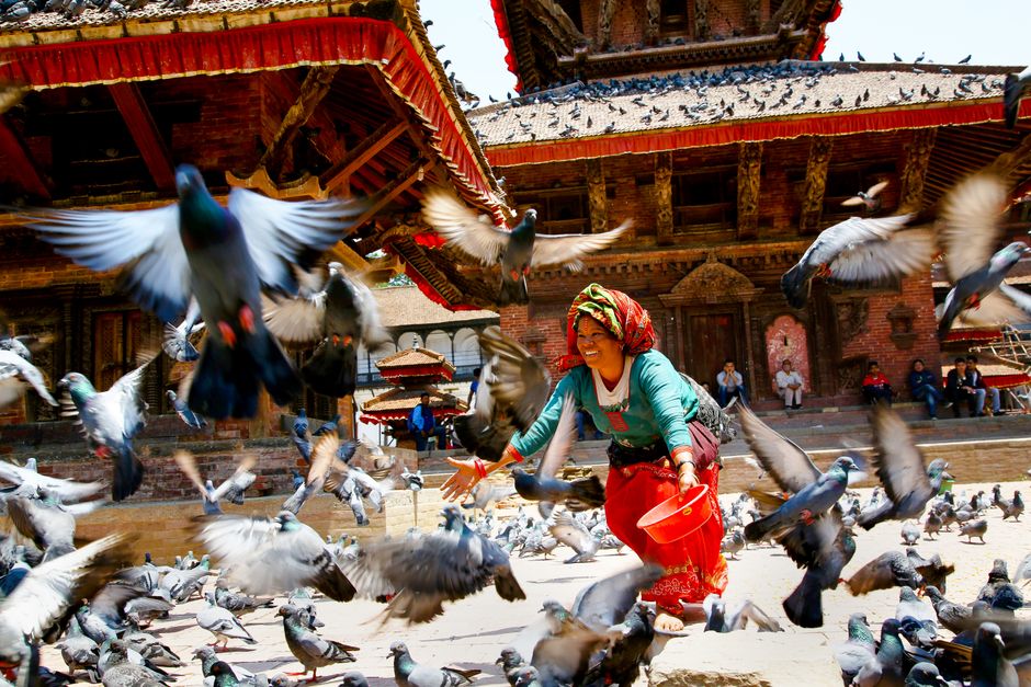 A joyful moment in Kathmandu Durbar Square with a woman feeding pigeons.
