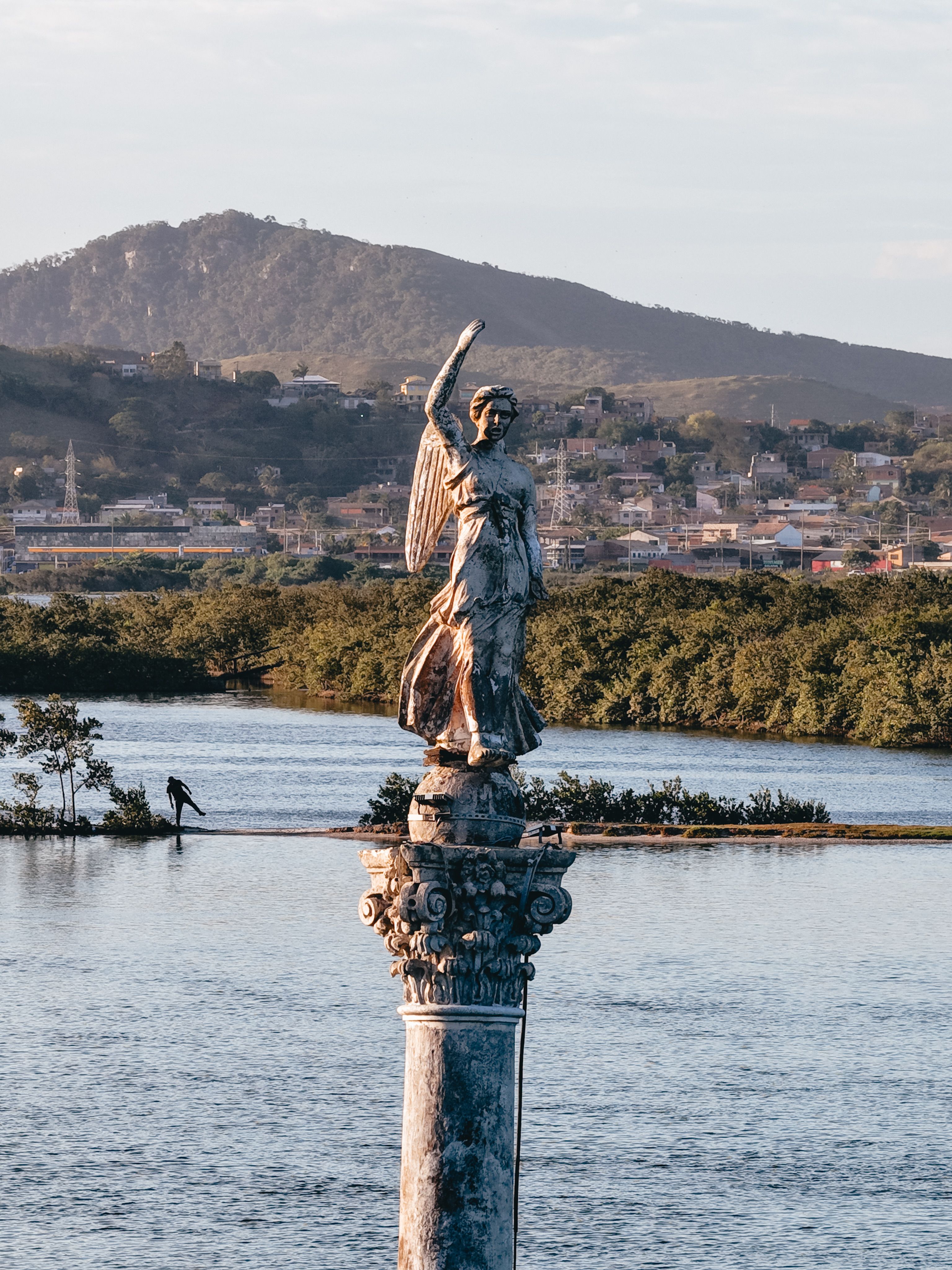 Statue Overlooking Coastal Town with Mountain View · Free Stock Photo