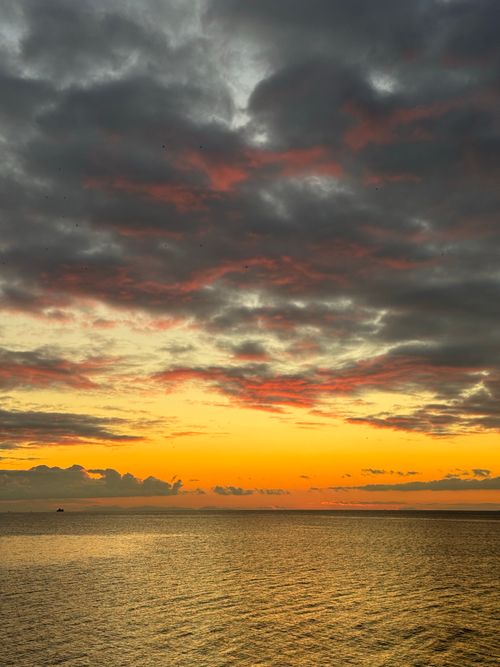Free Vibrant sunset with dramatic clouds over calm ocean horizon. Perfect for travel and nature visuals. Stock Photo