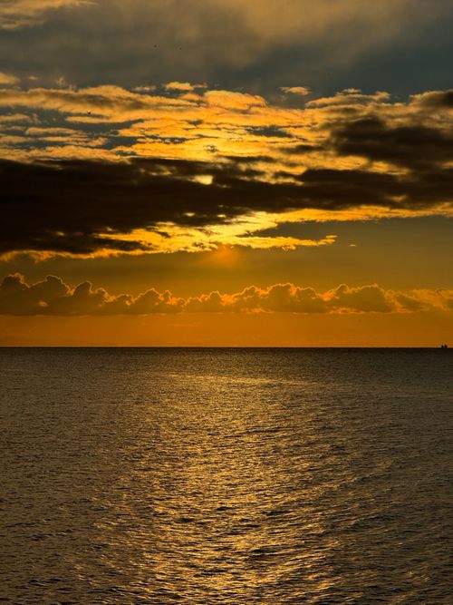 Free Golden sunset reflecting on the ocean with dramatic clouds in the sky. Stock Photo
