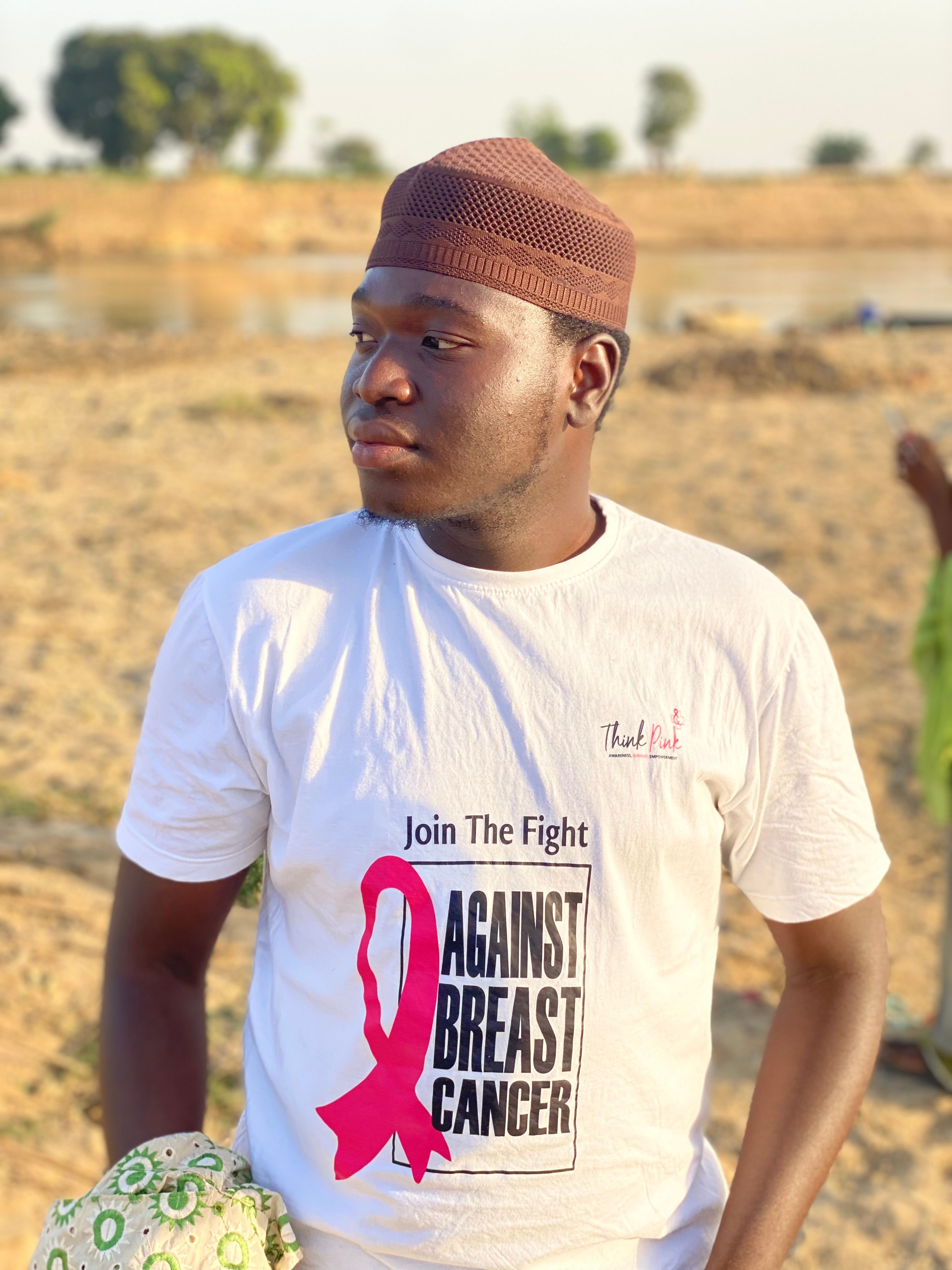 Young man wearing a t-shirt promoting breast cancer awareness outdoors in a sunny setting.