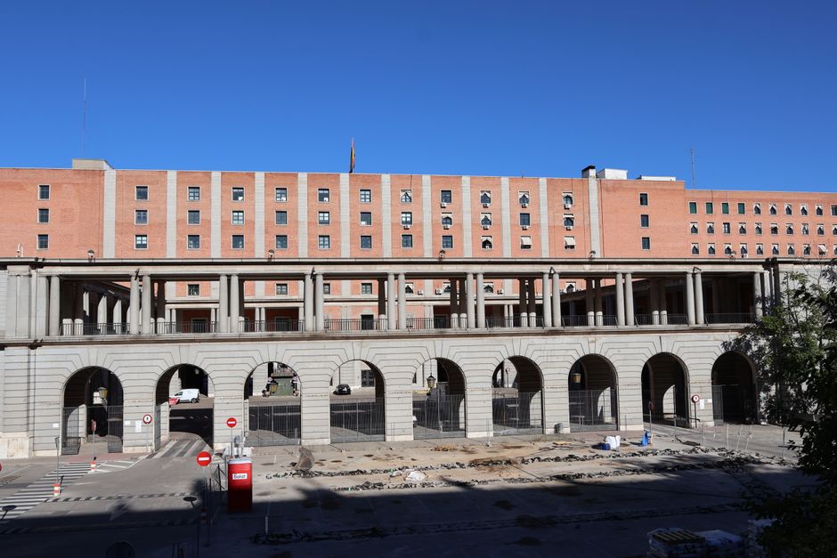 Vista de un edificio histórico con arcos y una pasarela en un día soleado en Madrid.