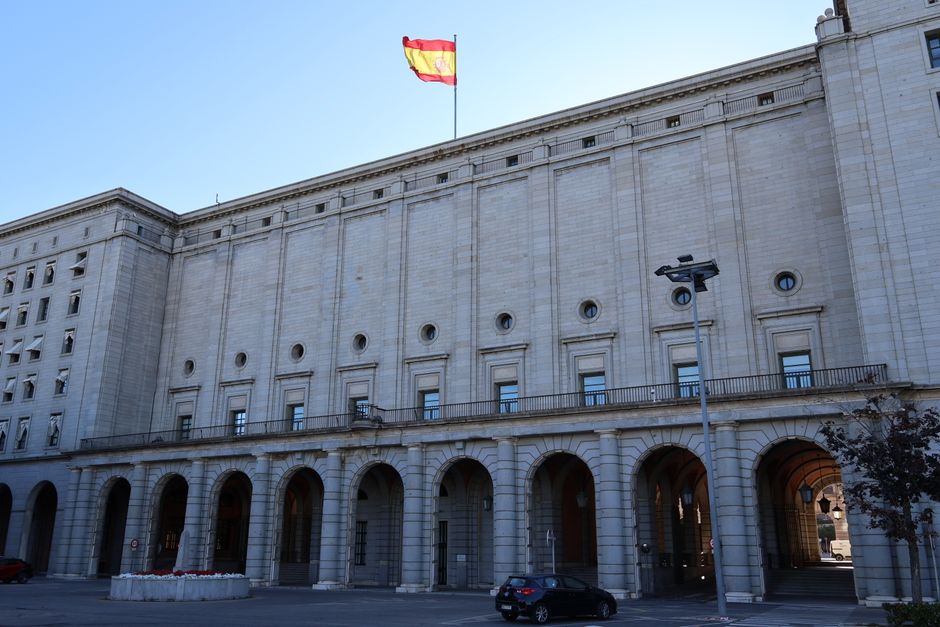 Exterior de un edificio gubernamental histórico en España con una bandera española en la cima.