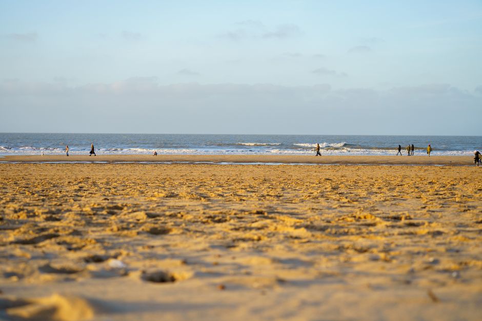 A tranquil beach with people strolling along the shoreline during the day.