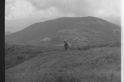 grey scale photo of a man walking towards a hill