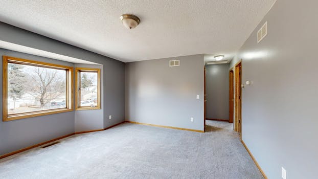 Bright empty room with large windows and grey carpet. Ideal for real estate listings.