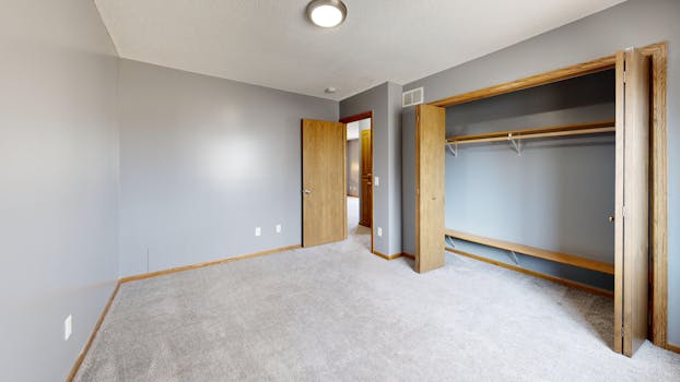 Spacious empty room with open closet, wooden doors, and grey walls.