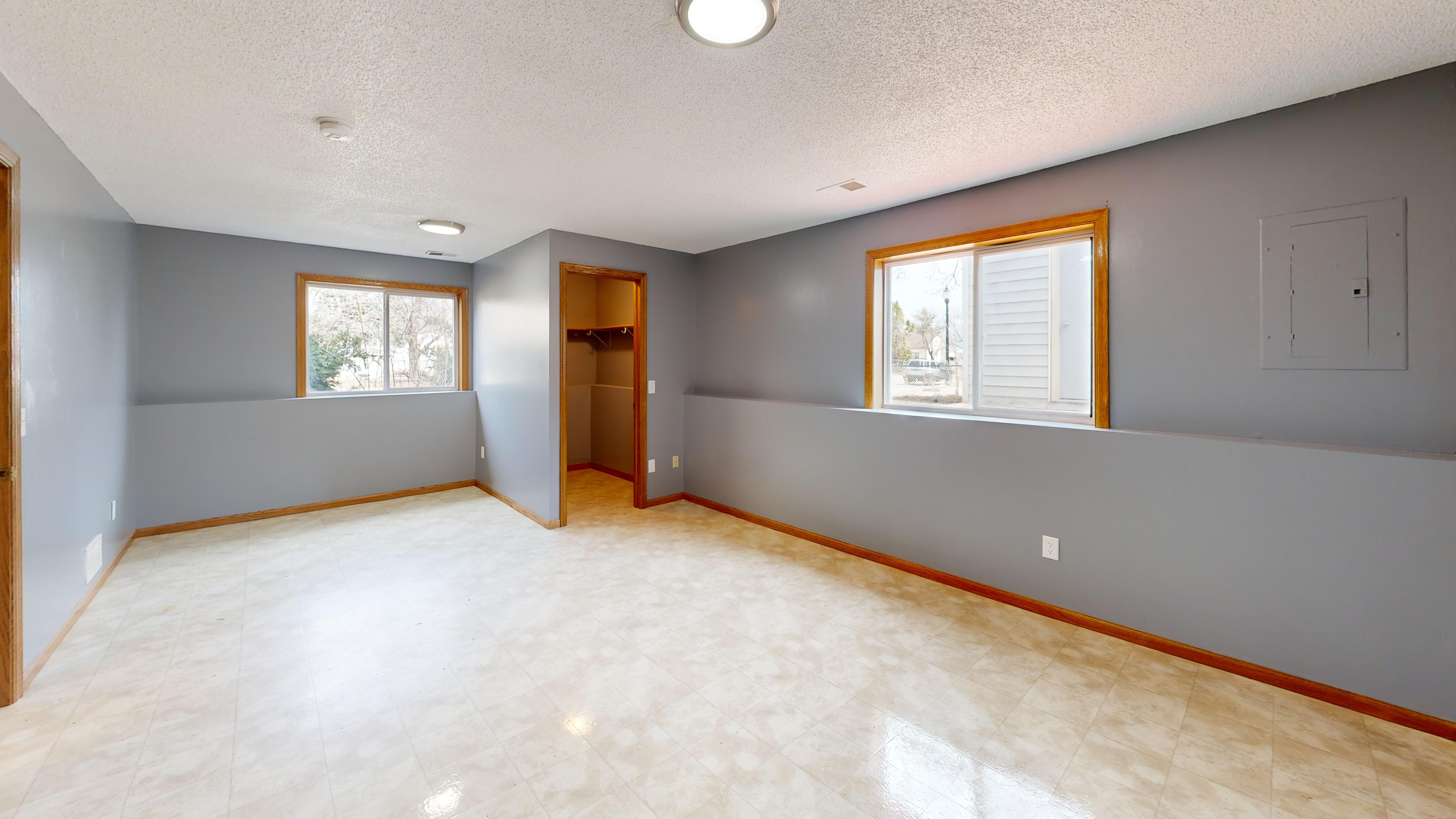 Alt Text: A spacious, empty modern room with light wood floors, clean white walls, natural sunlight streaming in from a window, and an open closet.