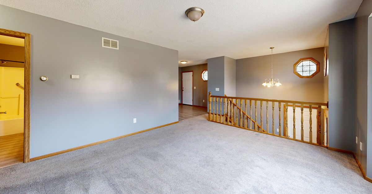 A bright, empty living room with carpet, wood accents, and natural light.