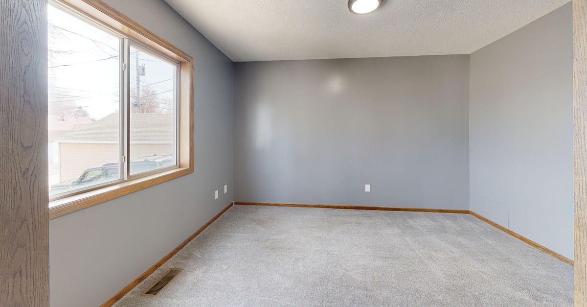 Spacious empty room with carpet, window, and neutral tones.