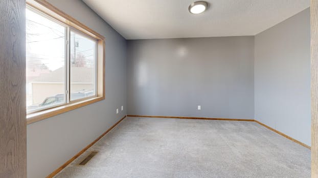 Spacious empty room with carpet, window, and neutral tones.