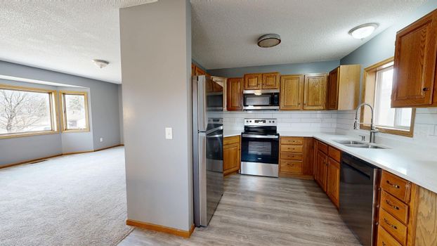 Bright kitchen and living space with wooden cabinets and stainless appliances.